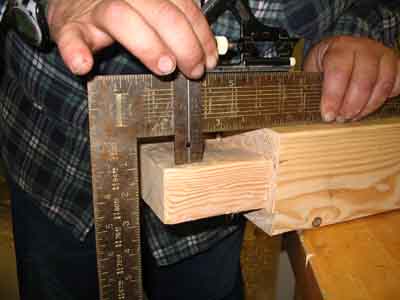 Checking a Tenon for parallel.
In this photo we see a framing square on the reference face of the piece. And a combination square on top of the framing square. The depth set on the combination square ruler is for the width of the framing square and the depth of the offset. This way we can check the entire surface of this tenon and see if it's offset the correct amount.
