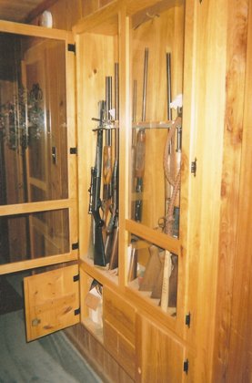 Cypress gun cabinet built into hall wall behind book shelves in den.
